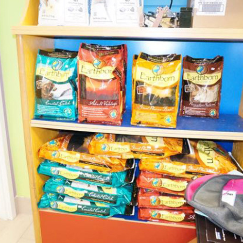 Shelves display colorful Earthborn dog food bags in teal, red, and yellow. The setting is neat and well-stocked, evoking a sense of organization.