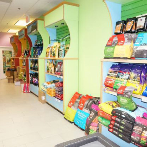 Colorful pet store aisle with shelves filled with various dog food bags in bright packaging. Shelving units are painted in pastel hues.