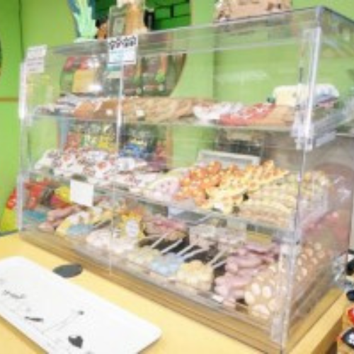 A glass display case showcases various colorful pastries and sweets in a bakery. The vibrant arrangement sits against a lively green wall, creating a cheerful atmosphere.