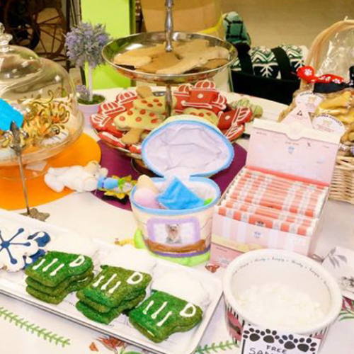 A colorful pet-themed dessert table featuring bone-shaped cookies, paw print trays, and bright green treats. The setup conveys a playful, joyful atmosphere.