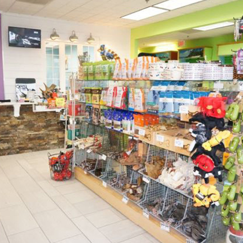 Pet store interior with brightly lit aisles filled with pet supplies. Shelves display treats and toys. Front desk in the background, creating a welcoming vibe.