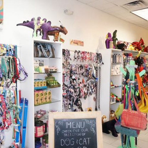 Pet store interior with colorful leashes, toys, and treats on shelves. A chalkboard sign promotes dog and cat products. Playful, inviting atmosphere.