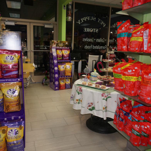 Pet store with neatly arranged shelves of colorful pet food bags. A table with a floral cloth displays pet treats, creating a welcoming, cozy atmosphere.
