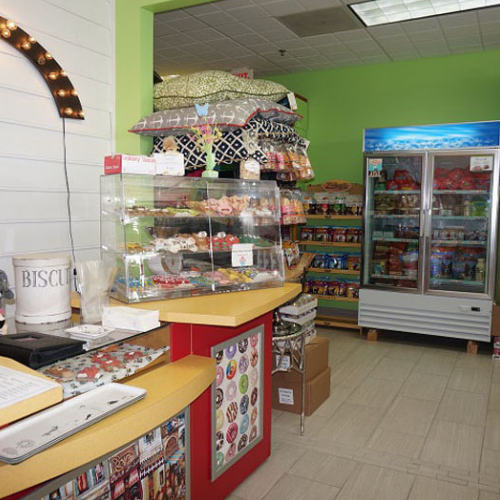 A cozy pet store interior with a counter displaying treats, shelves with colorful pet food bags, and stacked pet beds. Bright, welcoming atmosphere.