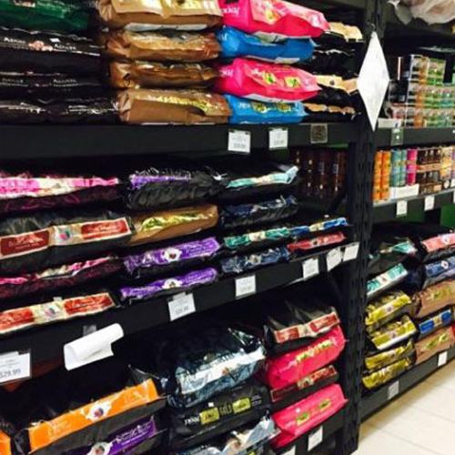 Shelves filled with colorful bags of pet food line a store aisle. Various brands and types are displayed, suggesting a wide selection for pet owners.