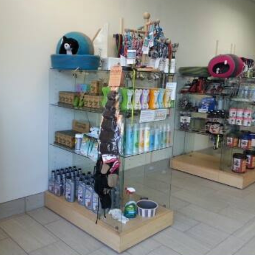 Pet supply store with glass shelves displaying assorted pet products, including cat beds, toys, shampoos, and food. Bright, organized, inviting atmosphere.