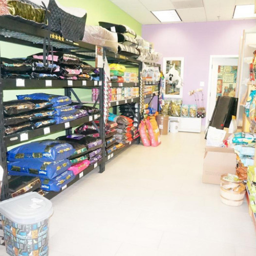 Pet store aisle with shelves displaying neatly stacked bags of pet food in various colors. Purple and green walls create a cheerful atmosphere.