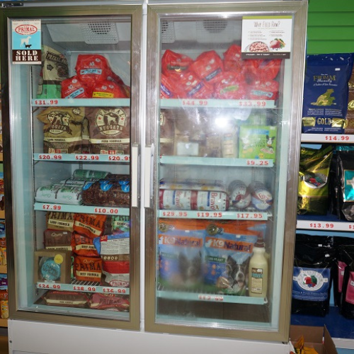 A pet food store freezer filled with various brands of raw and frozen pet foods, neatly organized in transparent bags with visible prices.