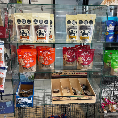 A colorful display of assorted dog toys on a white slat wall, including plush animals, donuts, and tug toys. The arrangement conveys a playful tone.